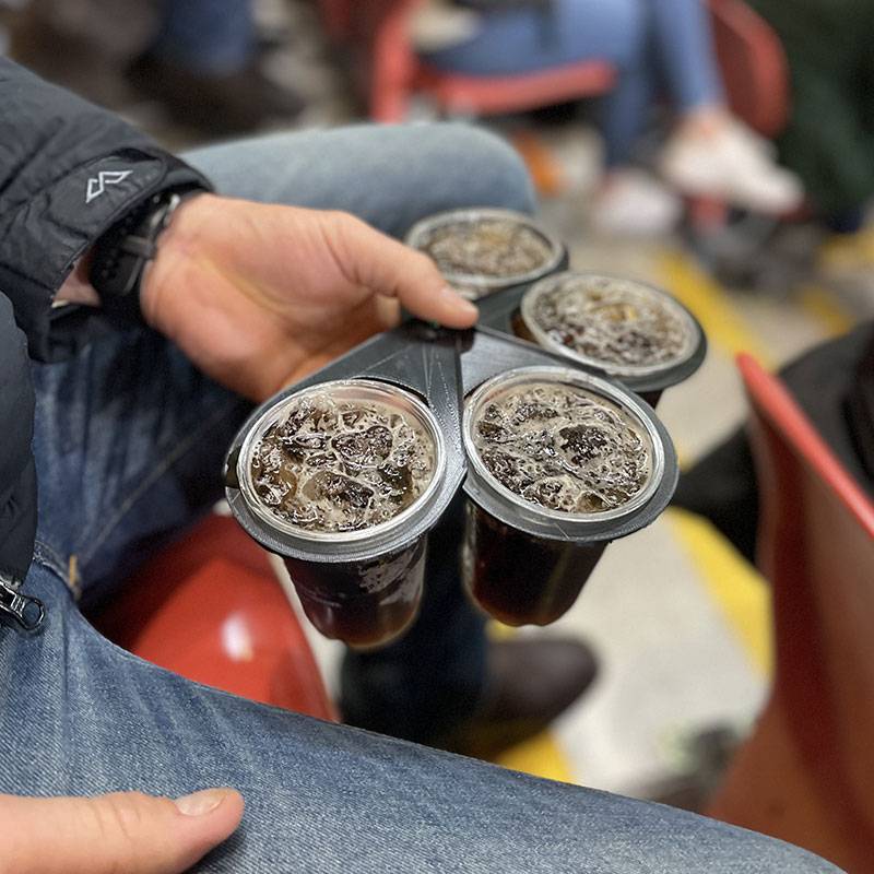 CarryMate environmentally friendly drink carrier, view from side, male sitting carrying four cups of soda and ice with black CarryMate built from recycled material